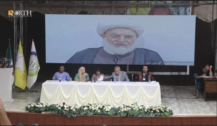 Una pantalla gegant mostra la intervenció del líder alauita Gazal Gazal.